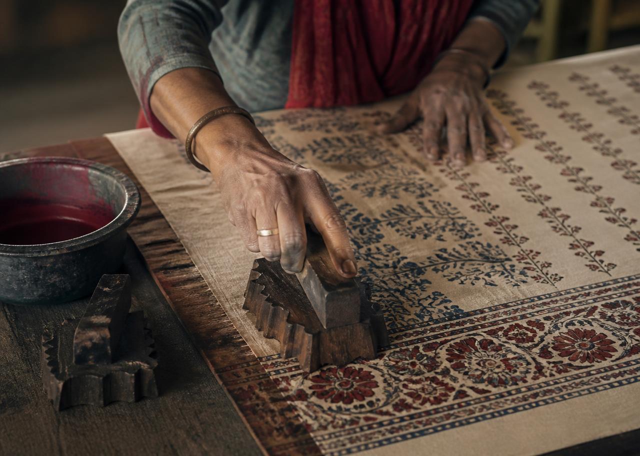 Hands printing a traditional block-printed textile on a wooden table